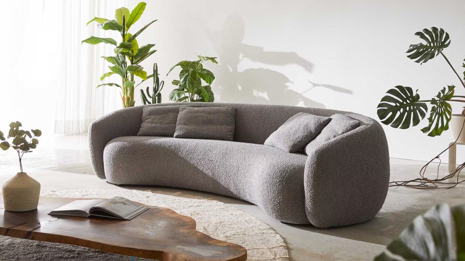 Organisch geformtes Sofa in "Bohnenform" mit einem Holztisch mit sanften Rundungen auf einem Teppich und Pflanzen im Wohnzimmer
