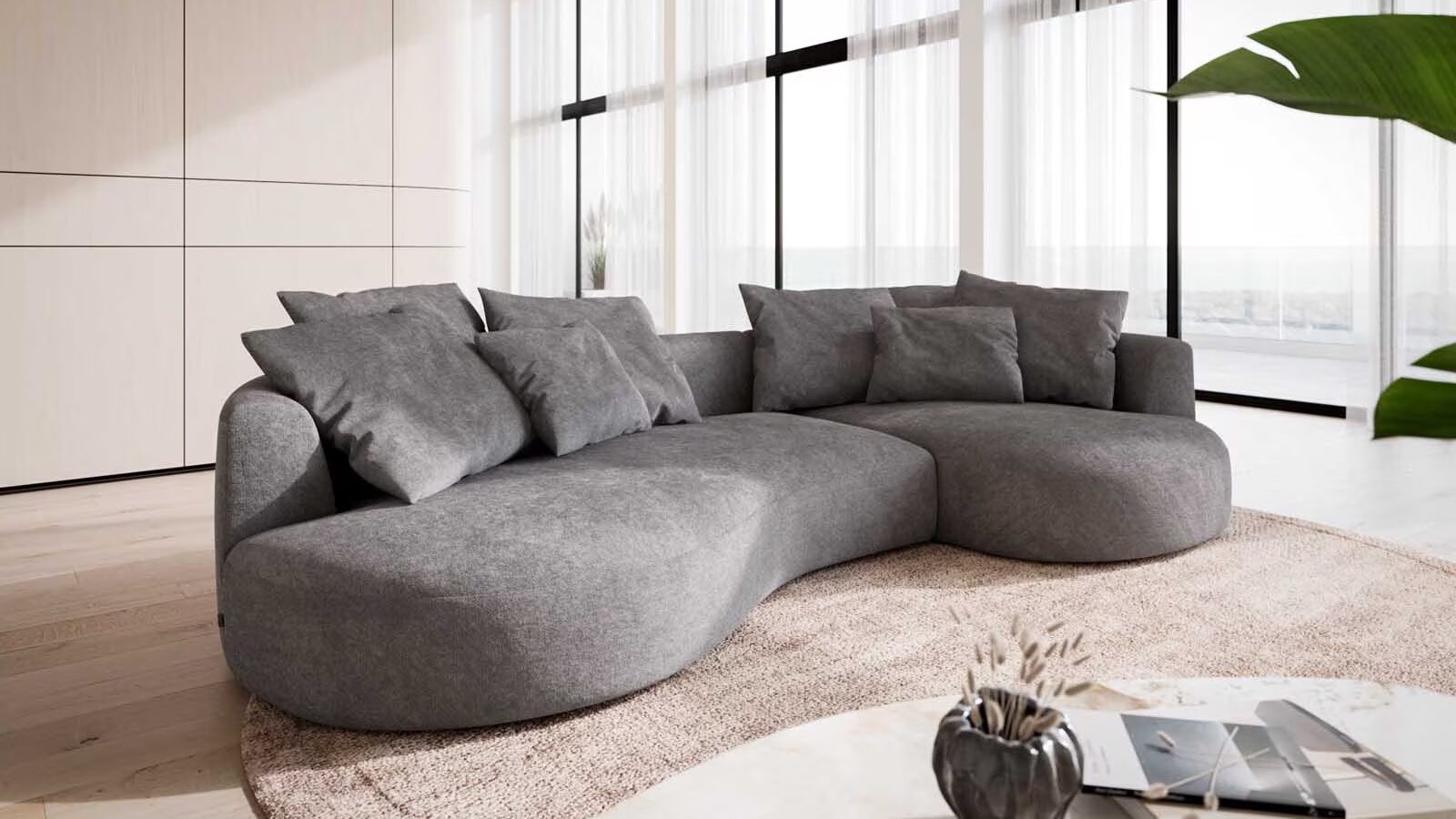 Wohnzimmer mit Sofa in organischer form vor großer Fensterfront auf rundem teppich mit einem couchtisch
