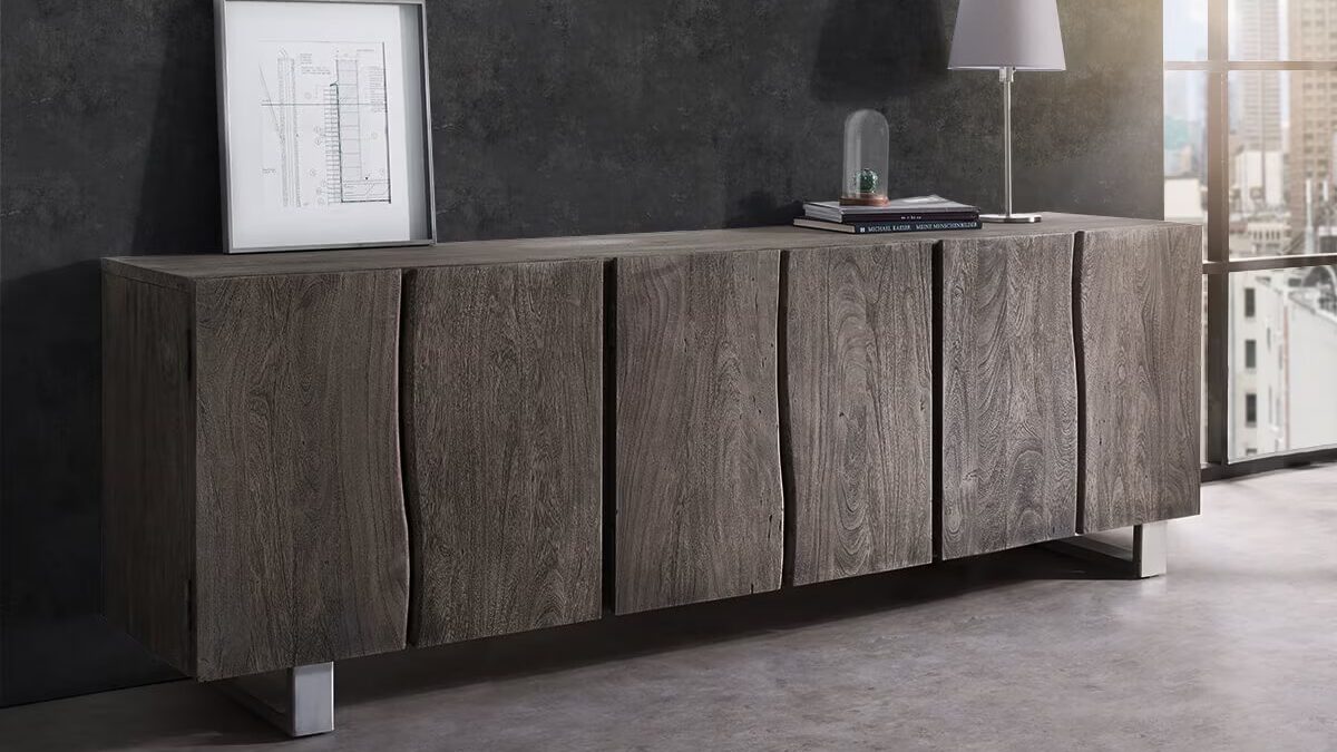 Massives Sideboard mit platin-farbenen Fronten aus Akazienholz mit sichtbarer Baumkante steht in einem Raum mit großem Fenster